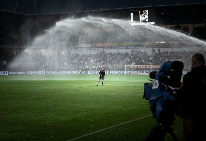 Fußballer im Stadion unter dem Regen der Bewässerunsanlage